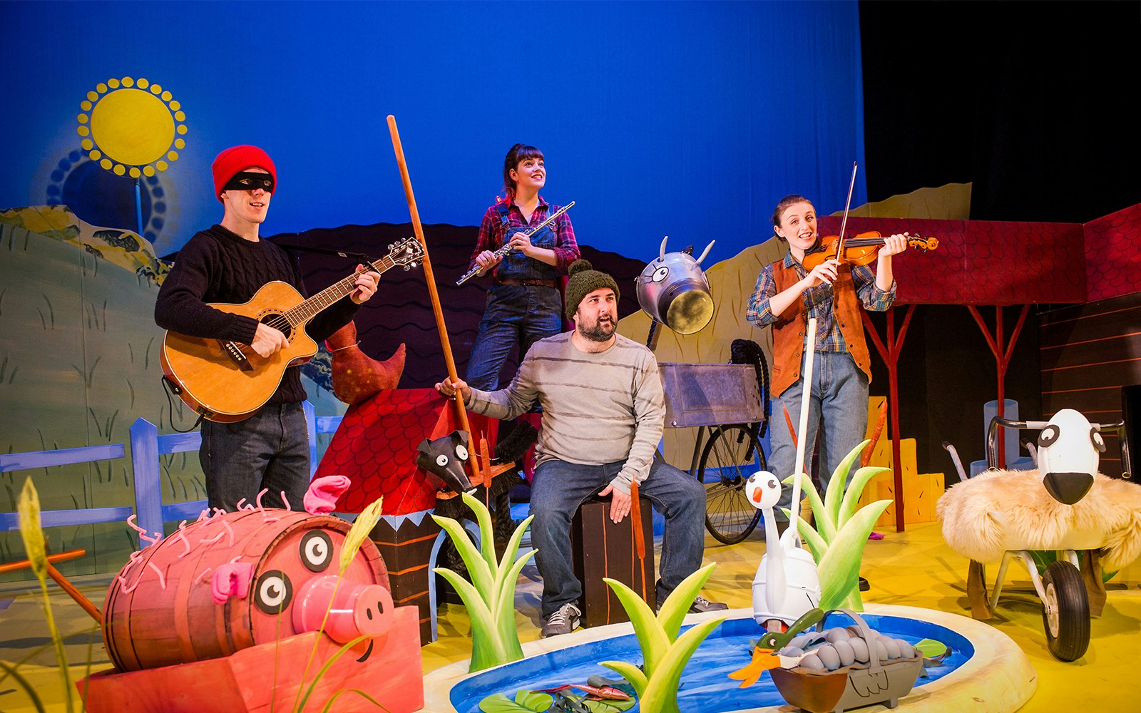 Stage performance of "What The Ladybird Heard" with actors and farm animal props.
