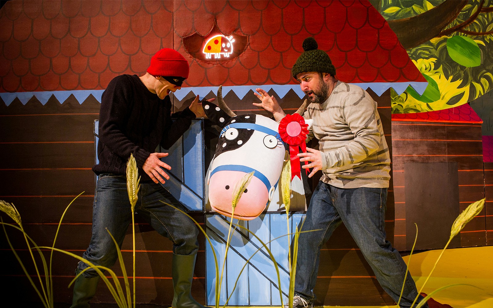 Two actors perform a scene with a cow puppet from "What The Ladybird Heard" show.
