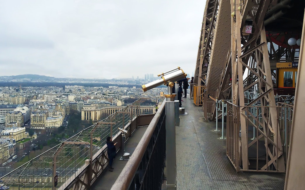 Eiffel Tower top floor view with telescopes overlooking Paris cityscape.