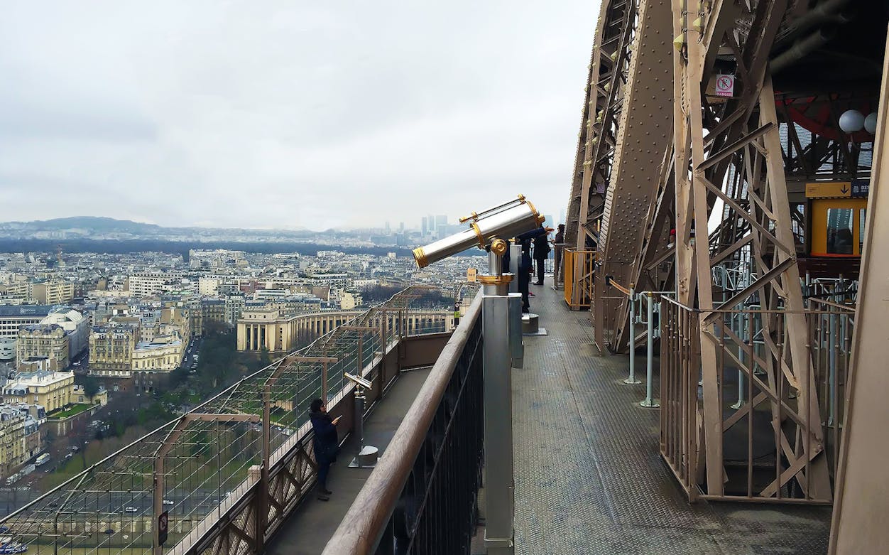 Eiffel Tower top floor view with telescopes overlooking Paris cityscape.