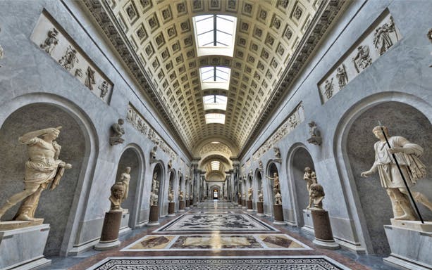Vatican Museums gallery with classical statues and ornate ceiling.