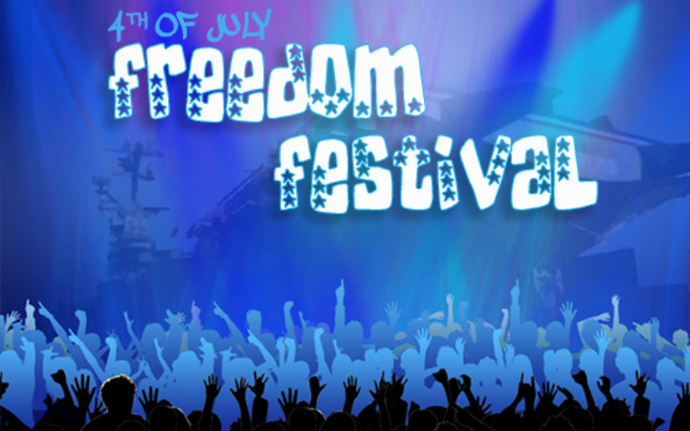 Crowd at Intrepid's Freedom Festival with vibrant lights and stage in the background.