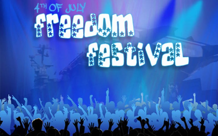 Crowd at Intrepid's Freedom Festival with vibrant lights and stage in the background.