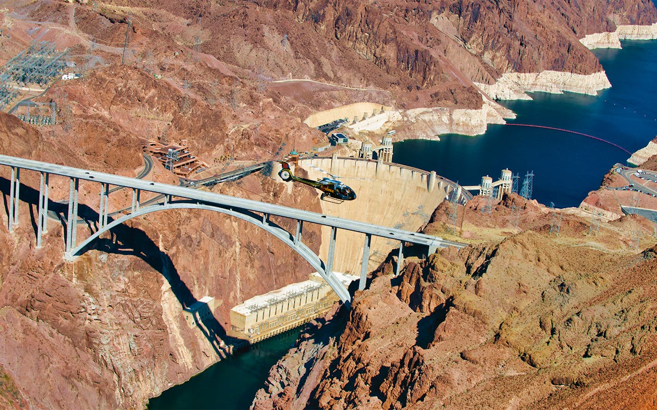 Aerial view of Hoover Dam with helicopter and bridge, part of Las Vegas bus tour.