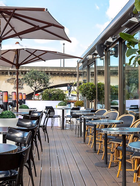 Outdoor seating at Le Bistro Parisien, Paris, with view of Seine River bridge.