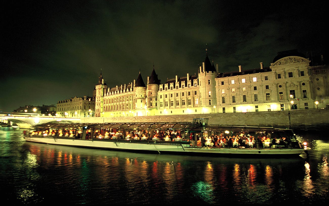 Bateaux Parisien cruise on Seine River with illuminated Conciergerie at night.