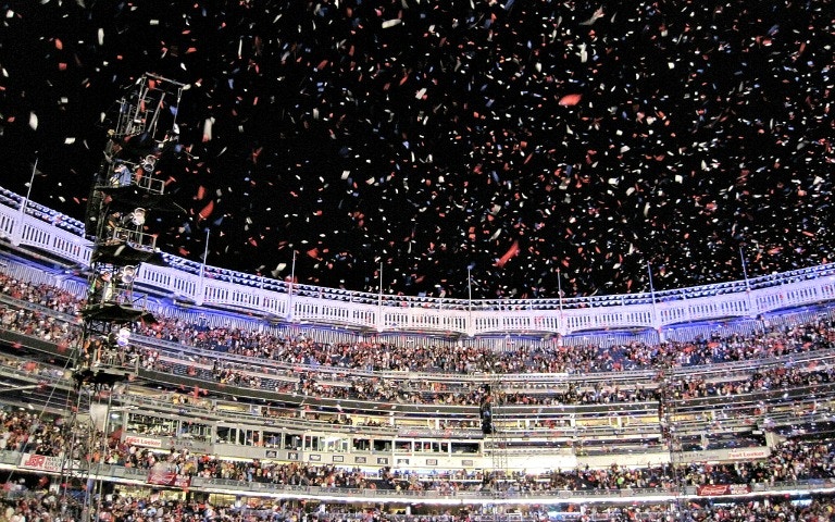 Crowd at Yankee Stadium with confetti falling during a night event.