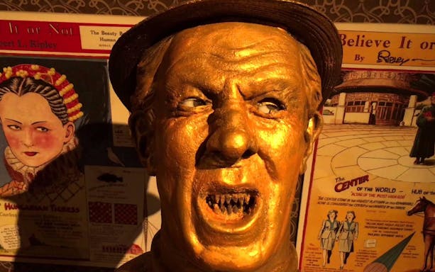 Golden statue with exaggerated features at Ripley's Believe It or Not, surrounded by vintage posters.