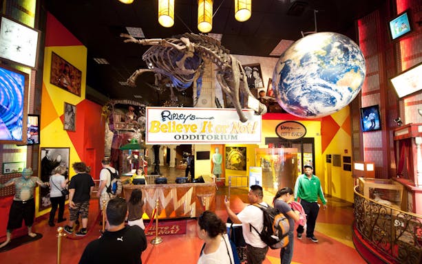 Visitors entering Ripley's Believe It or Not Odditorium with dinosaur skeleton and globe display.