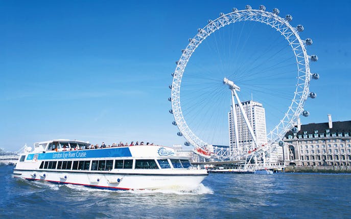 London Eye and river cruise boat on the Thames in London.