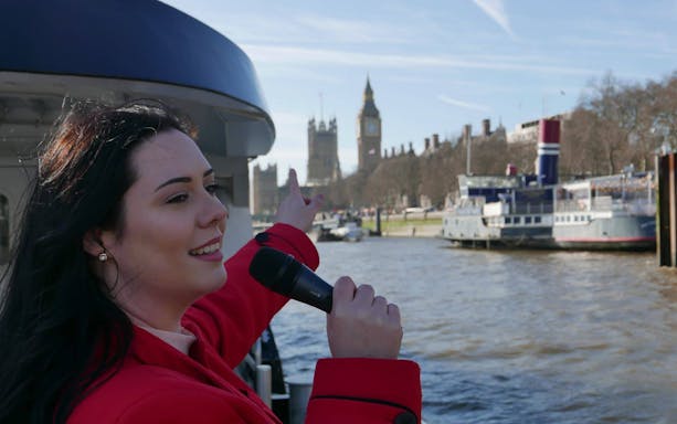 Tour guide pointing at Big Ben from a Thames cruise boat in London.