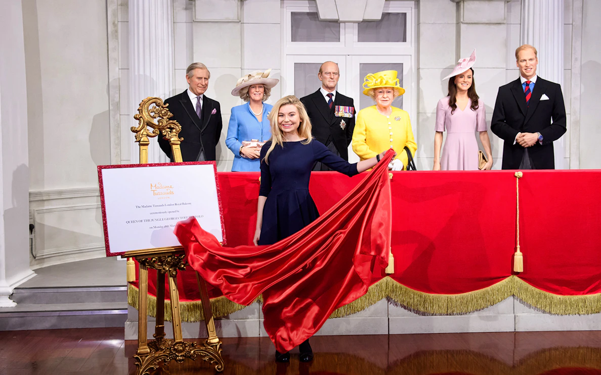 Madame Tussauds wax figures of British royals with a red curtain display.