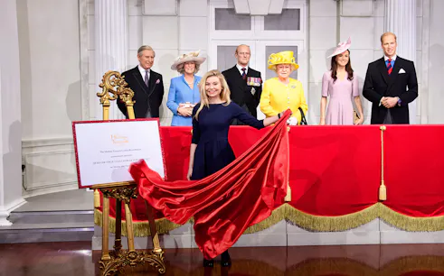 Madame Tussauds wax figures of British royals with a red curtain display.