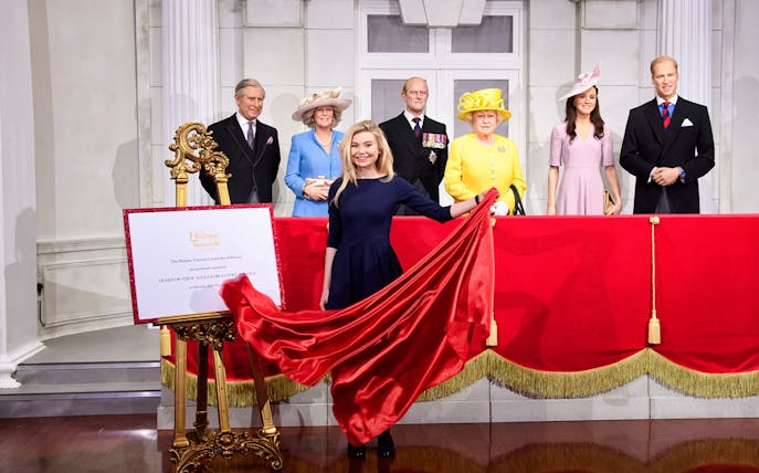 Madame Tussauds wax figures of British royals with a red curtain display.