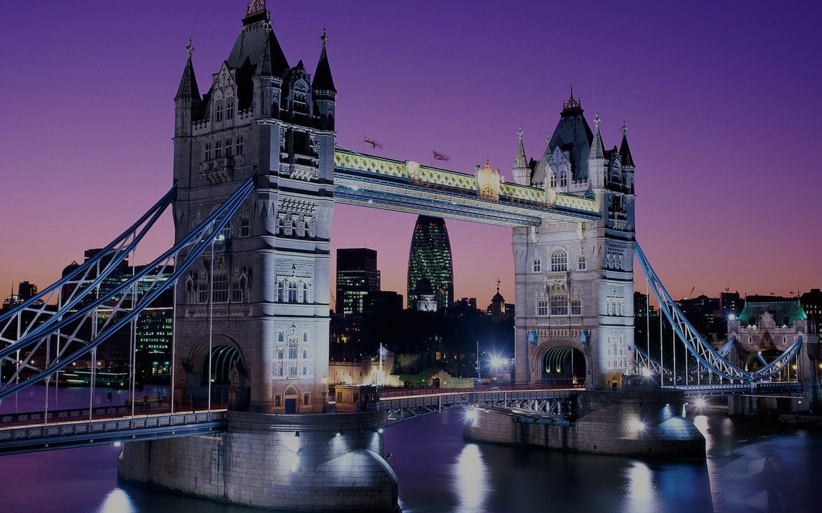 Tower Bridge illuminated at dusk with city skyline, London.