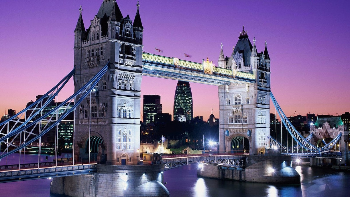 Tower Bridge illuminated at dusk with city skyline, London.