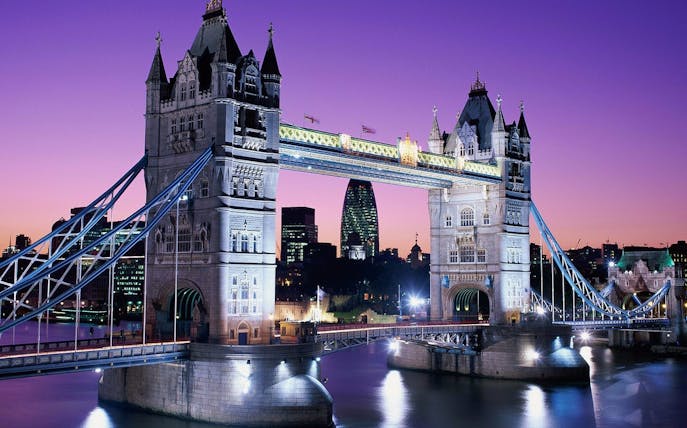 Tower Bridge illuminated at dusk with city skyline, London.