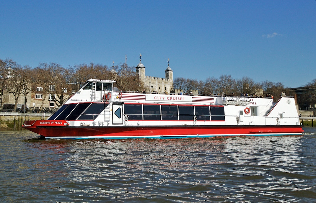 Red and white City Cruises boat on the Thames with Tower of London in the background.