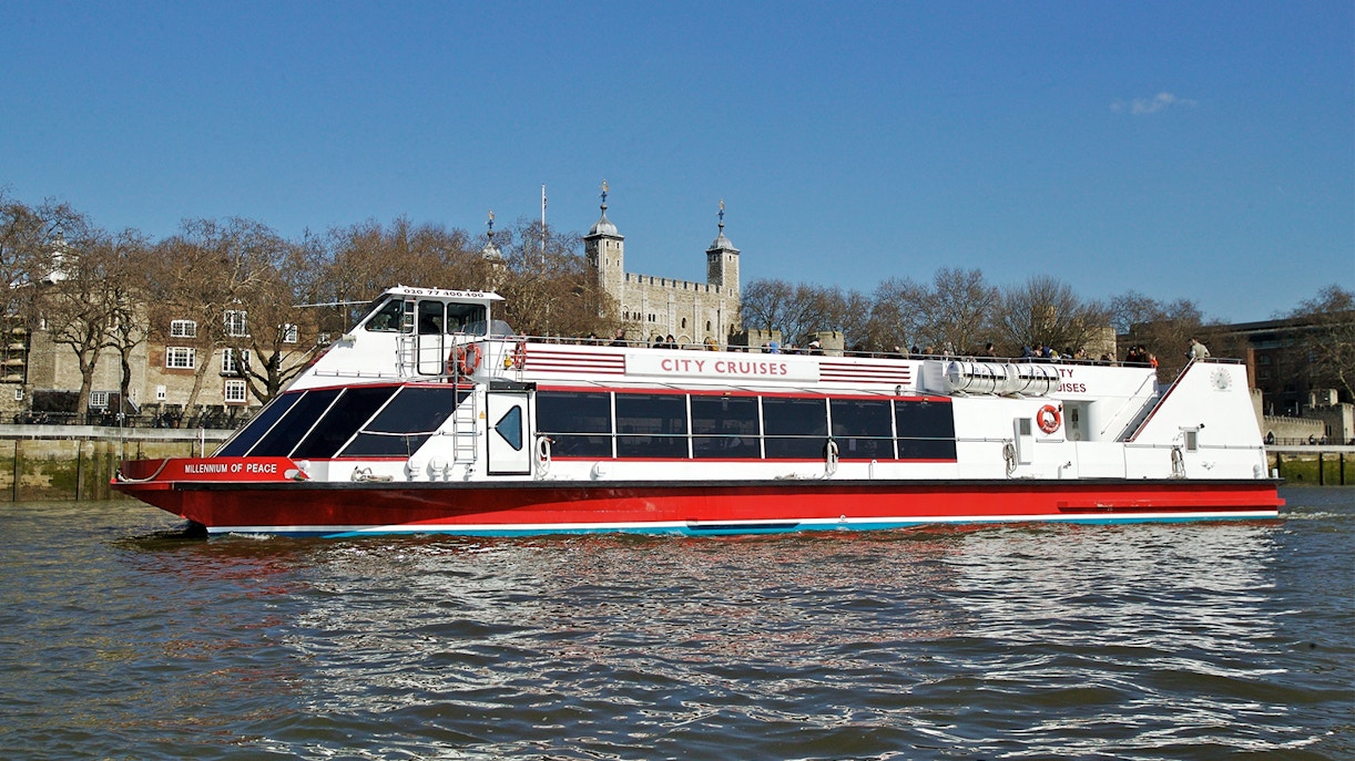 Red and white City Cruises boat on the Thames with Tower of London in the background.