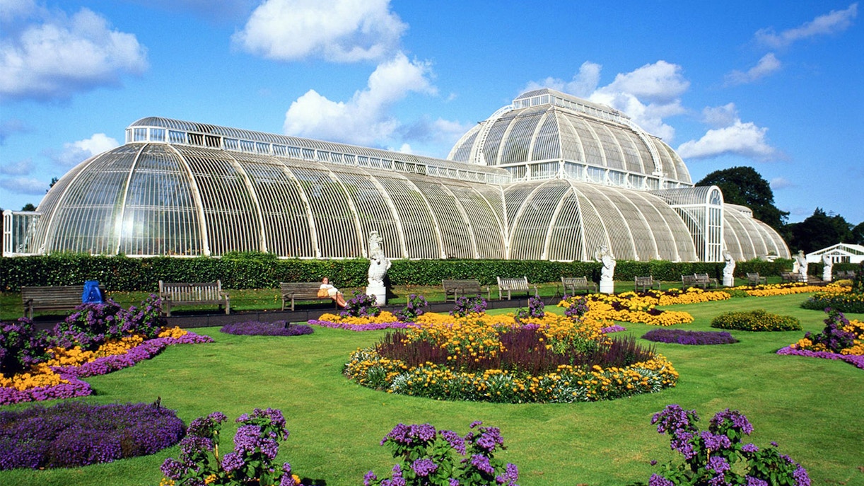 Kew Gardens glasshouse with vibrant plants, viewed from Thames River cruise in London.