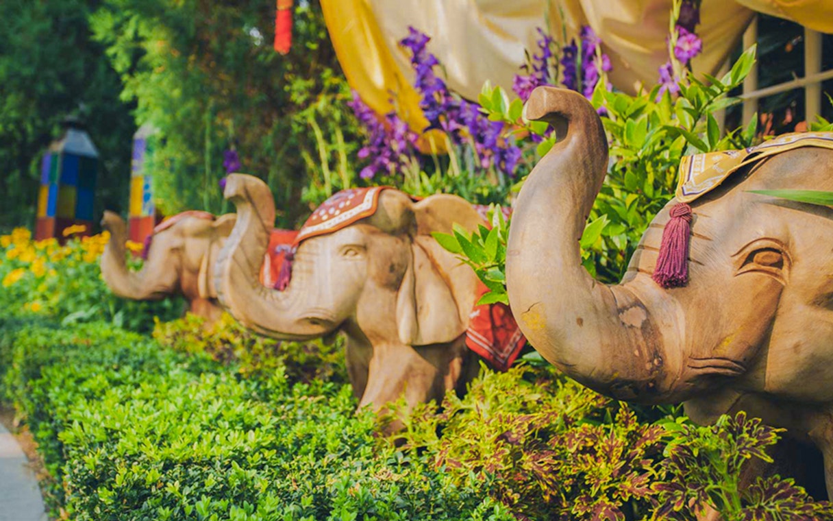 Wooden elephant sculptures surrounded by vibrant flowers at a garden attraction.