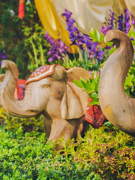 Wooden elephant sculptures surrounded by vibrant flowers at a garden attraction.