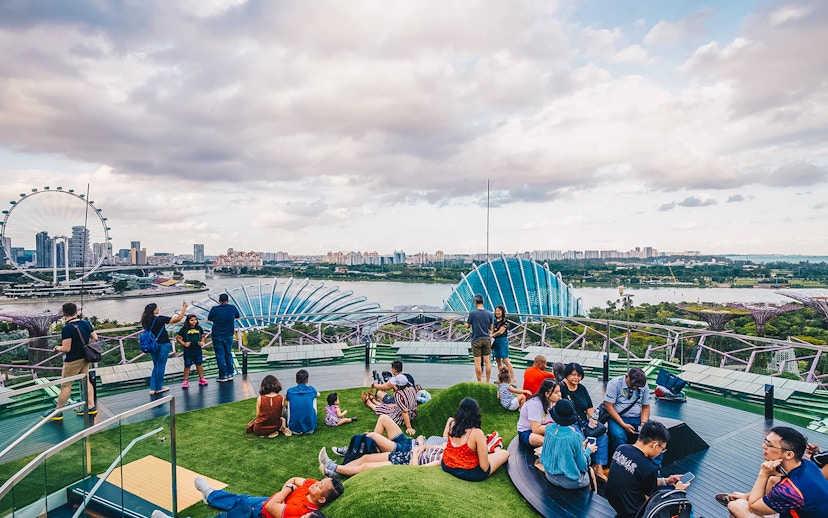 Visitors relaxing at Supertree Grove, Gardens by the Bay, Singapore, with OCBC Skyway and city skyline.