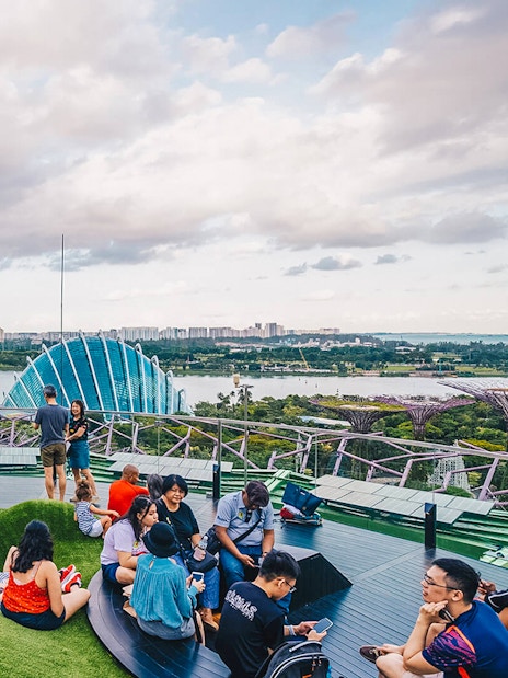 Visitors relaxing at Supertree Grove, Gardens by the Bay, Singapore, with OCBC Skyway and city skyline.
