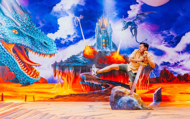 Man posing with sword in dragon-themed illusion at Singapore Trick Eye Museum.
