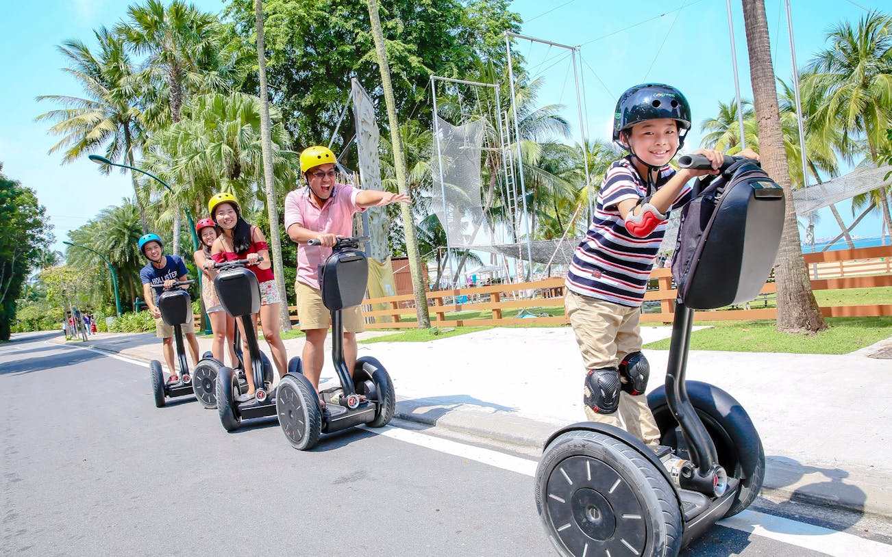 Group enjoying Segway ride on Sentosa Island path surrounded by palm trees.