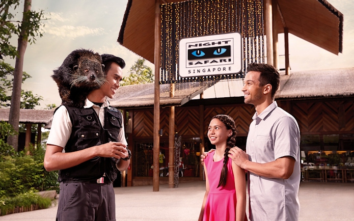 Guide with binturong on shoulder at Night Safari entrance, Singapore, interacting with visitors.