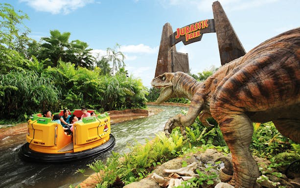 Visitors on a Jurassic Park ride at Universal Studios Singapore with a dinosaur model nearby.