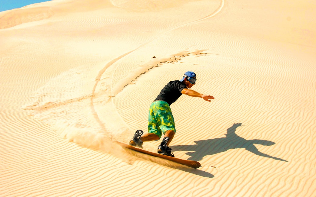 Person sandboarding on desert dunes during morning safari.