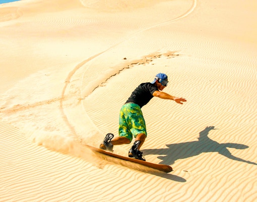 Person sandboarding on desert dunes during morning safari.
