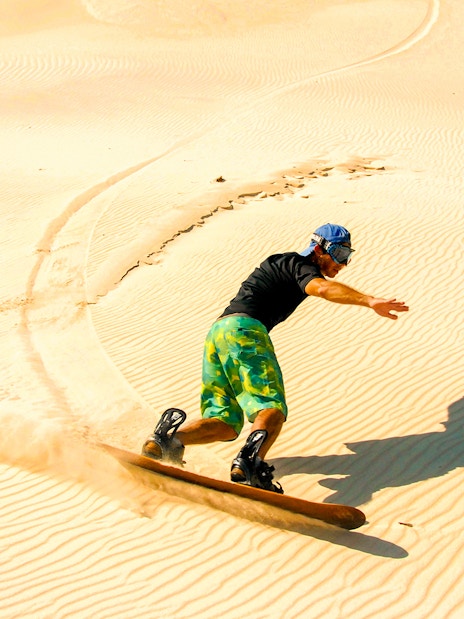 Person sandboarding on desert dunes during morning safari.