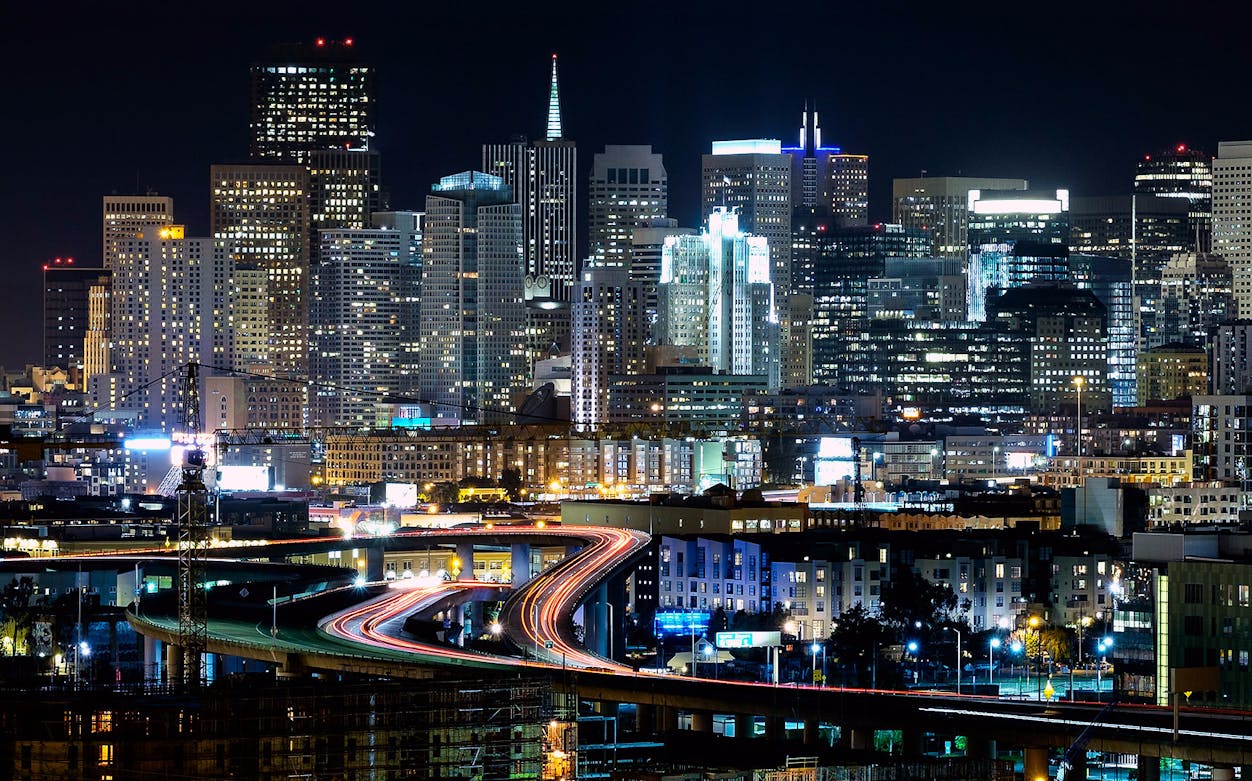 San Francisco skyline at night with illuminated skyscrapers and busy highway.