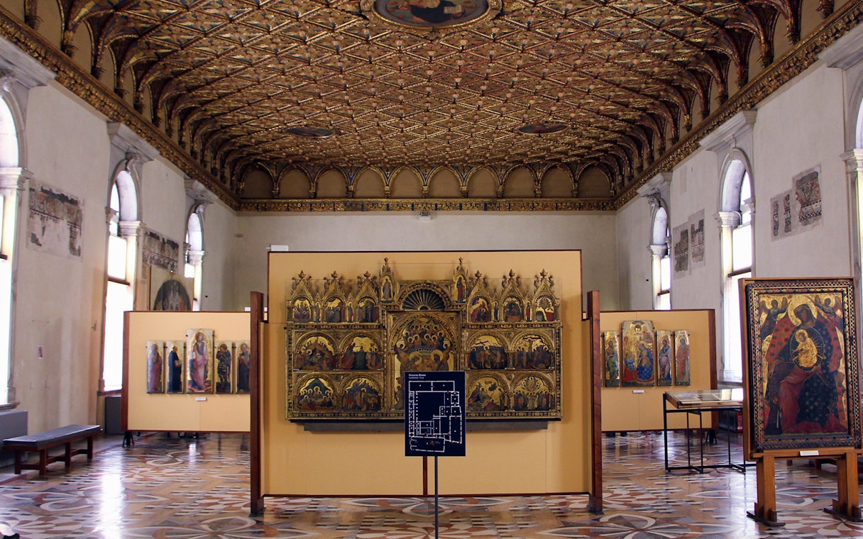 Visitors in Uffizi gallery viewing medieval religious artworks under ornate ceiling, Florence combo ticket.