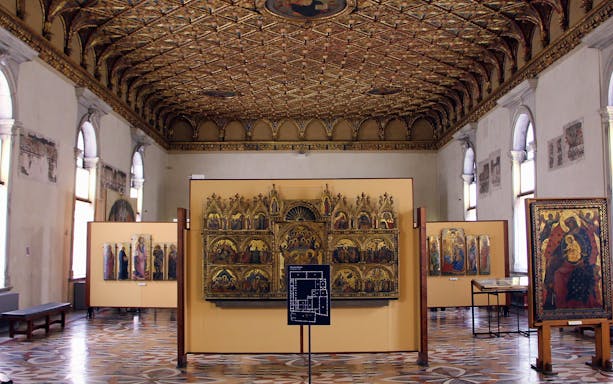 Visitors in Uffizi gallery viewing medieval religious artworks under ornate ceiling, Florence combo ticket.