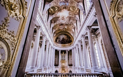 Versailles Palace interior with ornate columns and detailed ceiling fresco.