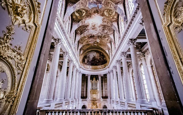 Versailles Palace interior with ornate columns and detailed ceiling fresco.