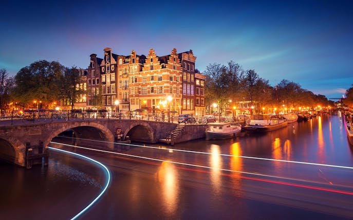 Evening canal cruise in Amsterdam with illuminated bridges and historic buildings.