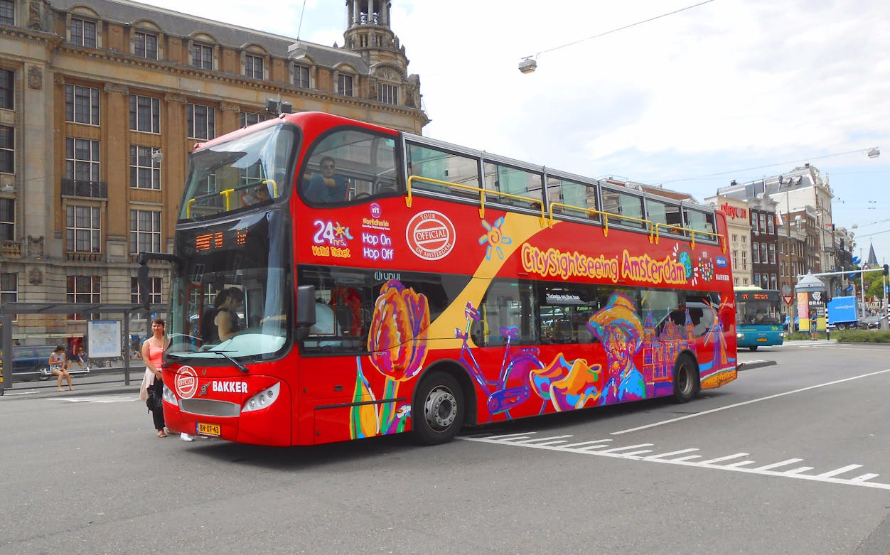 Hop-on hop-off sightseeing bus in Amsterdam near historic buildings.