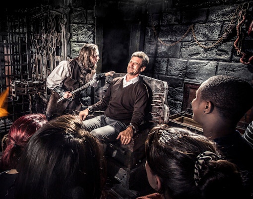 Man in medieval torture scene at Amsterdam Dungeon with onlookers.