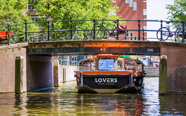 Semi-open boat passing under a bridge on an Amsterdam canal.