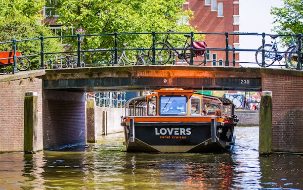 Semi-open boat passing under a bridge on an Amsterdam canal.