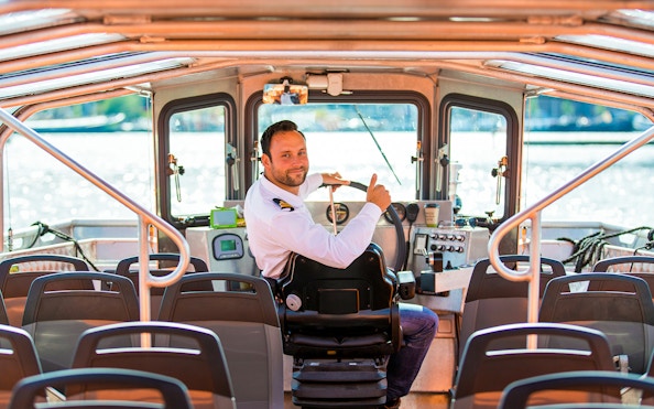 Boat captain steering semi-open cruise in Amsterdam.