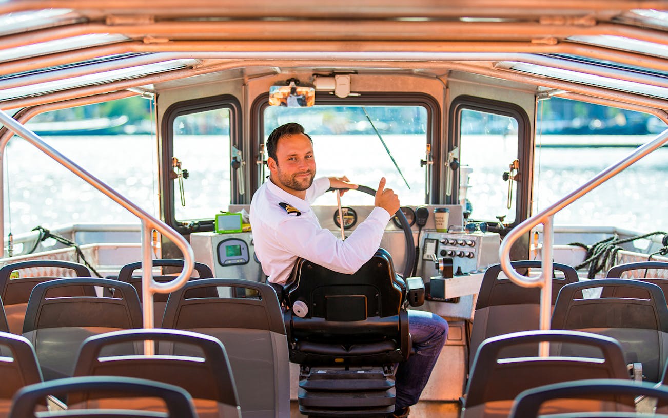 Boat captain steering semi-open cruise in Amsterdam.