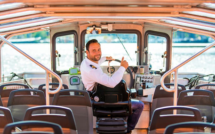 Boat captain steering semi-open cruise in Amsterdam.