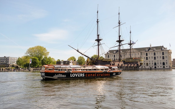 Semi-open boat cruise passing the Amsterdam Maritime Museum and historic ship.