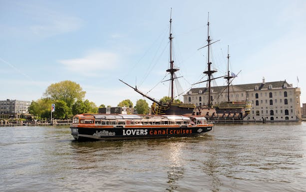 Semi-open boat cruise passing the Amsterdam Maritime Museum and historic ship.